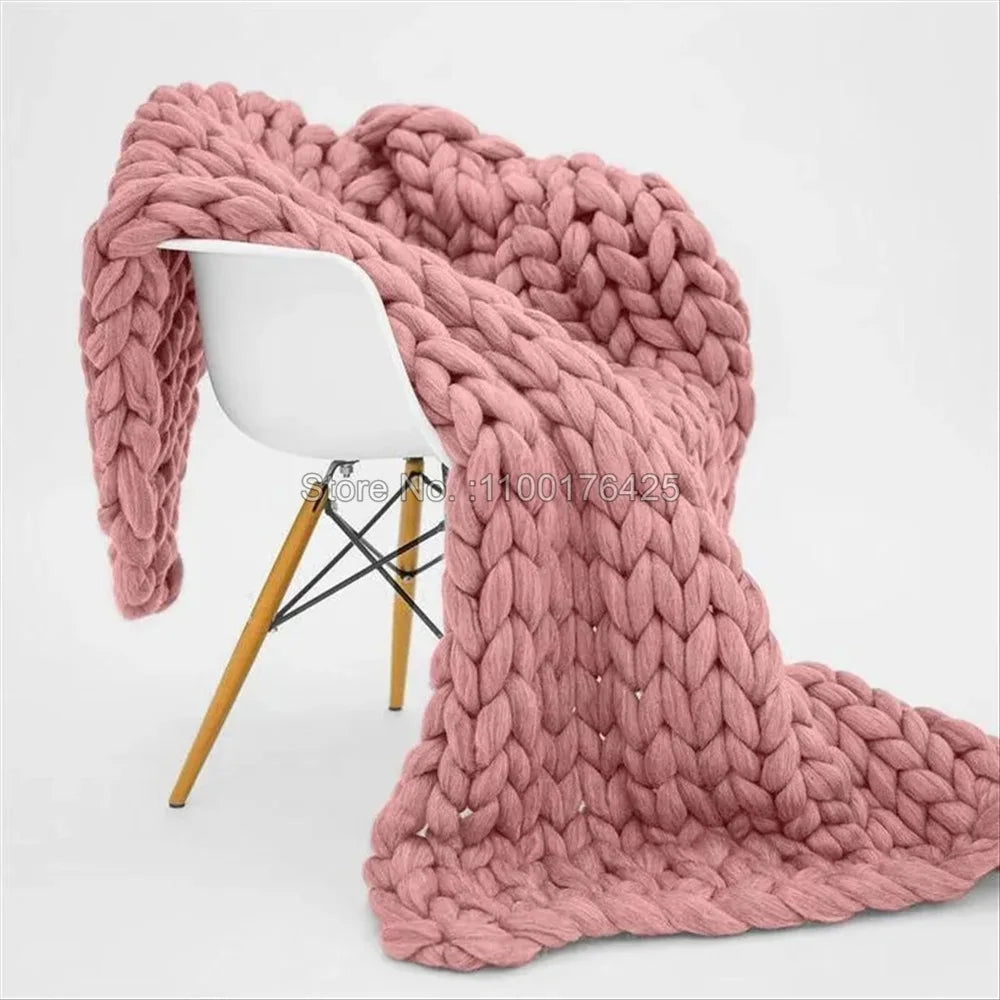 Pink chunky hand-knitted yarn blanket draped over a modern white chair.