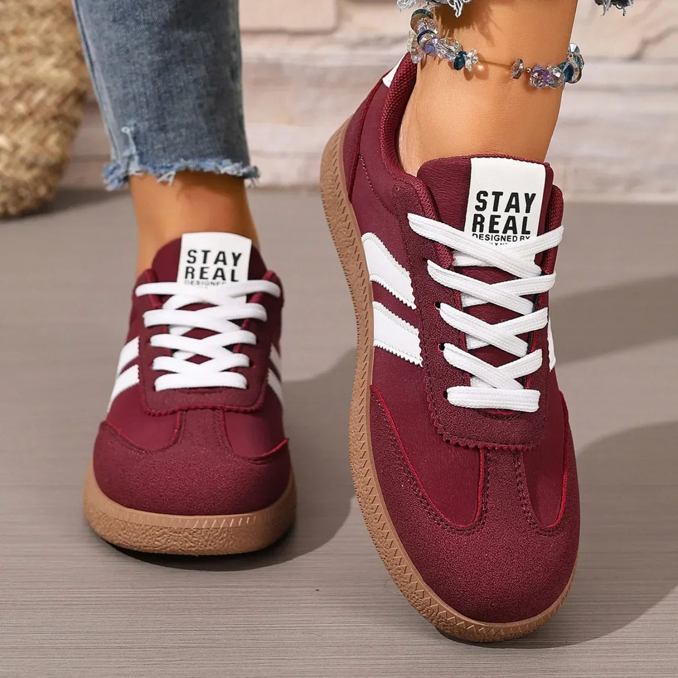 Maroon faux leather slip-on sneakers with white laces, a brown textured sole, and Stay Real tongue branding for walking.