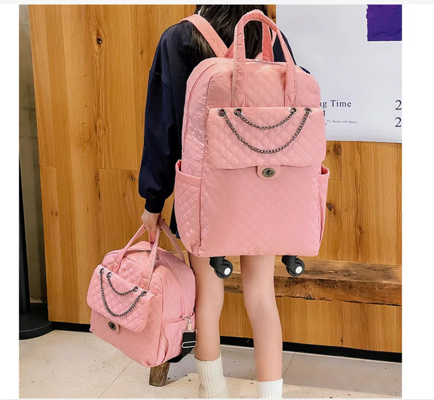 Pink quilted rolling backpack and matching handbag with chain accent and wheels.
