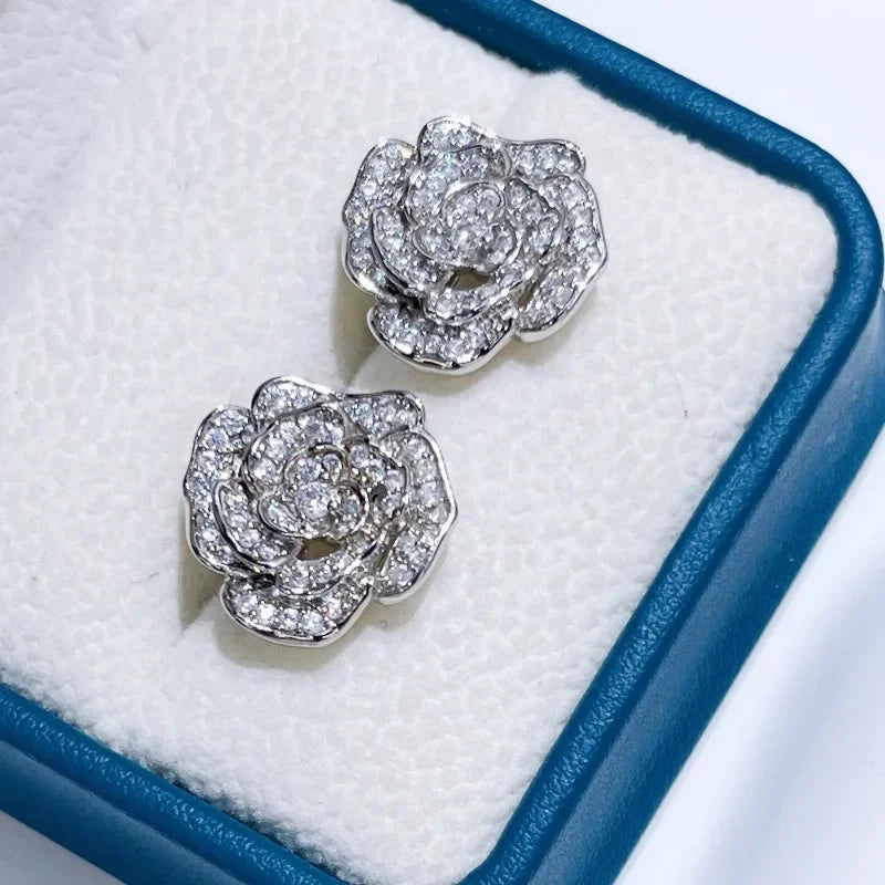 Silver-tone camellia flower stud earrings encrusted with sparkling cubic zirconia stones in a jewelry box.