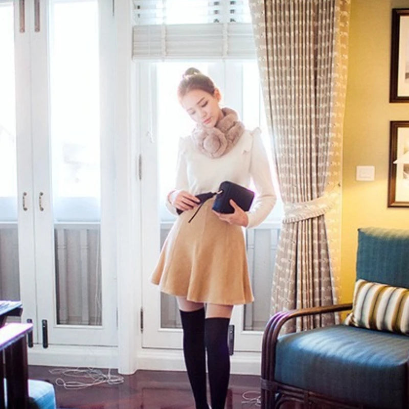 Thick beige rabbit fur triple-tube winter scarf with a pom pom detail, worn by a woman.
