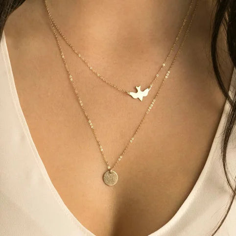 Gold-colored metal layered necklace with a dove pendant and a round textured coin pendant.