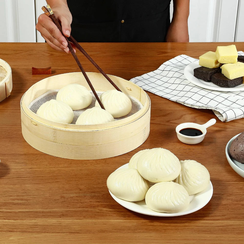 Natural bamboo steamer basket holding white steamed buns, with chopsticks picking up a bun.