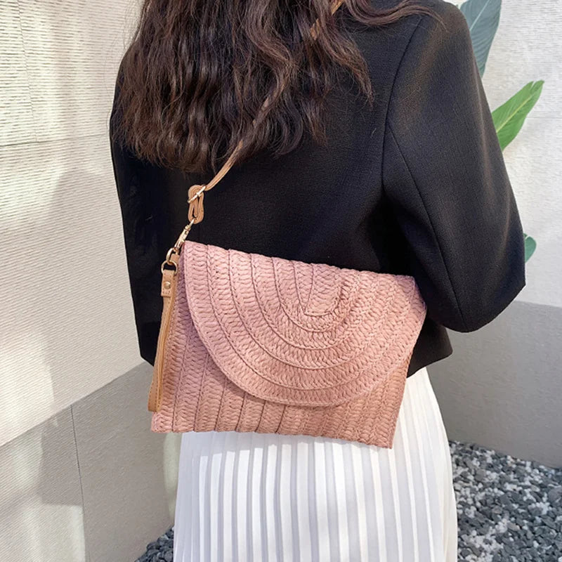 Pink straw envelope crossbody bag with an adjustable strap, used as a summer beach purse.