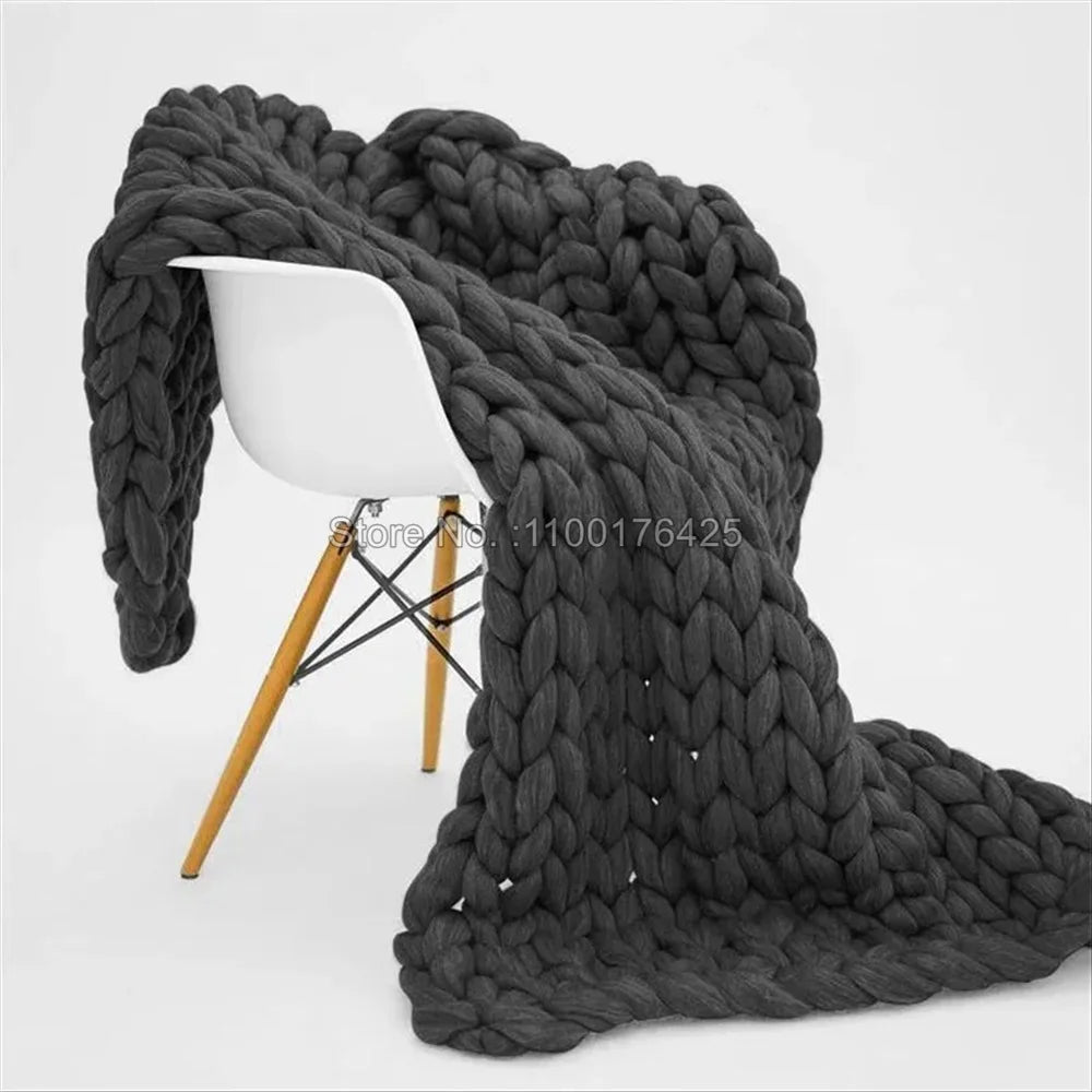 Dark gray chunky knit blanket draped over a modern white chair with wooden legs.