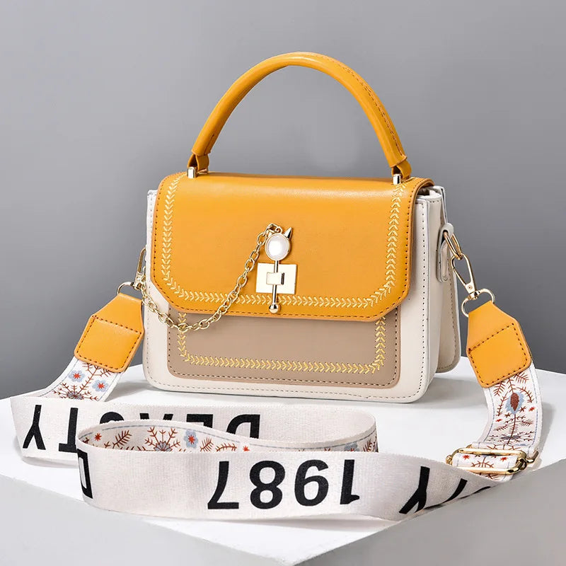 Yellow, white, and tan leather structured handbag with top handle and a decorative chain and clasp.