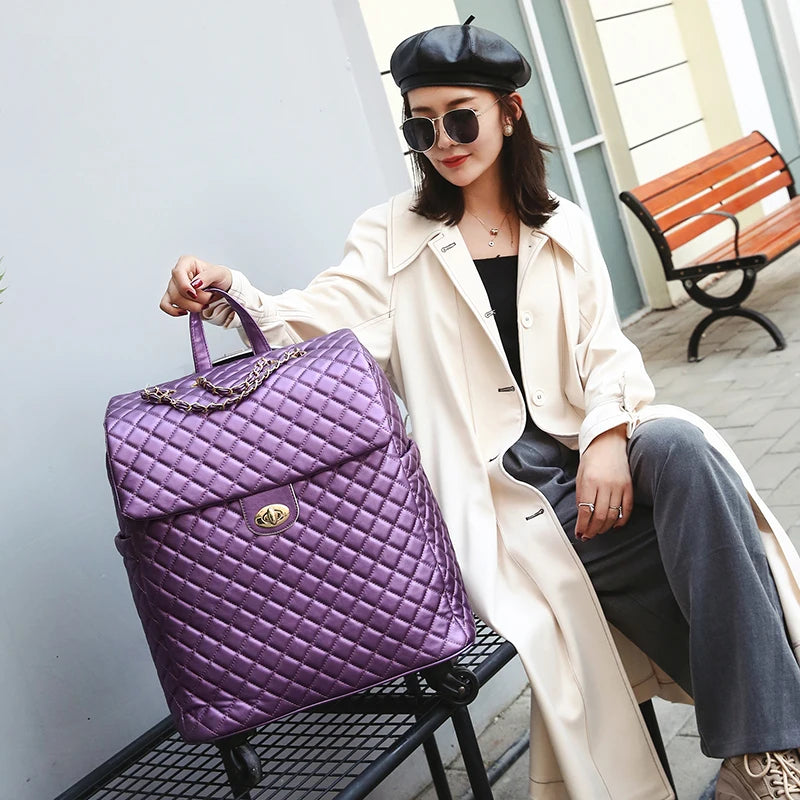 Purple quilted PU rolling suitcase with a gold turn-lock closure, top handle, and chain detail.