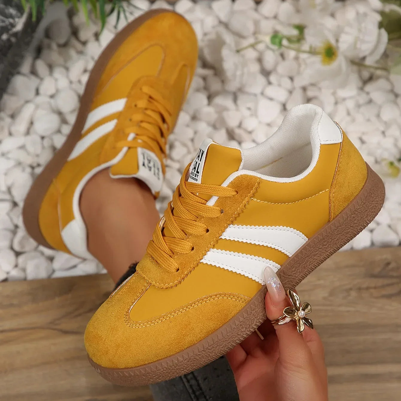 Mustard yellow leather and suede slip-on sneakers with white stripes, white heel tabs, and brown gum rubber soles.