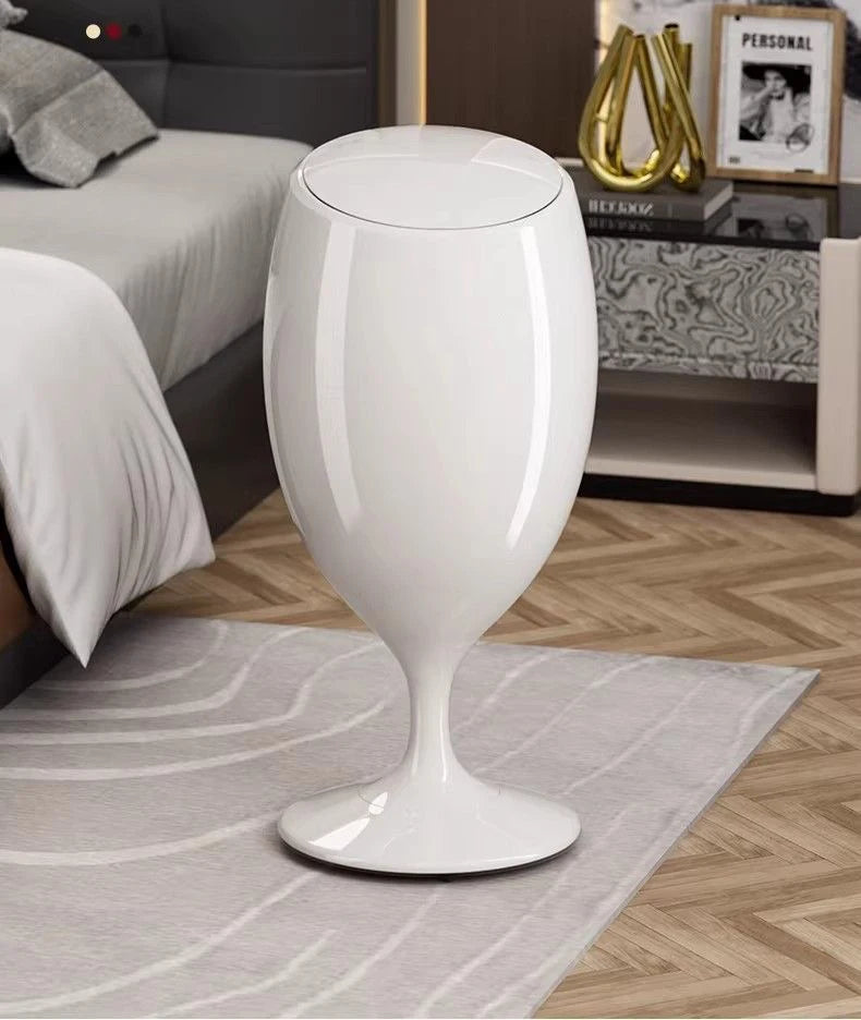 Glossy white wine-glass shaped trash can standing on a rug in a bedroom.