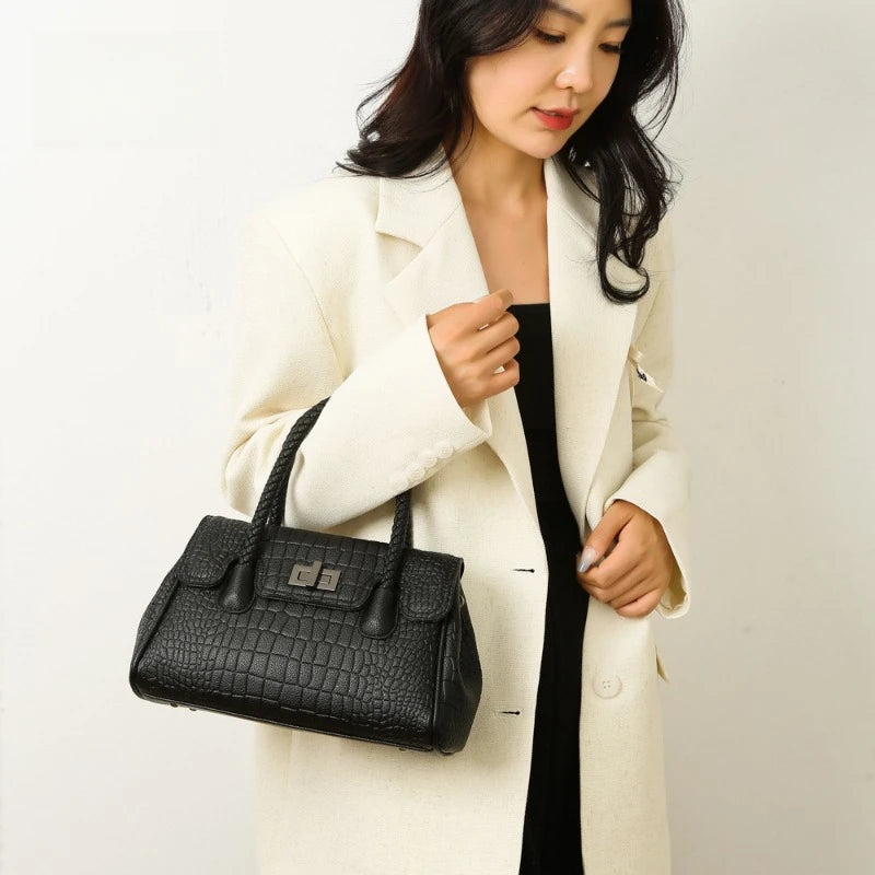 Black crocodile-pattern faux leather handbag with braided handles and twist lock, used for everyday work.