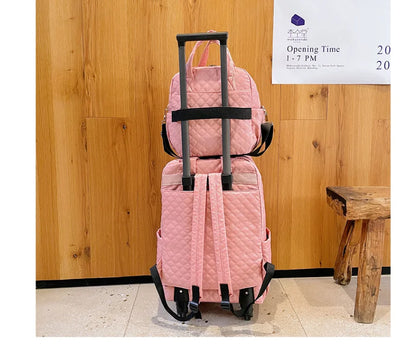 Pink quilted rolling backpack and matching handbag set on a telescoping handle.