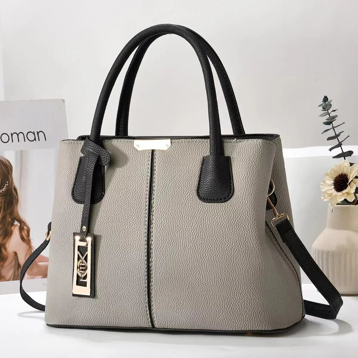 Grey faux leather structured tote bag with black handles, gold accents, and zip closure for everyday use.
