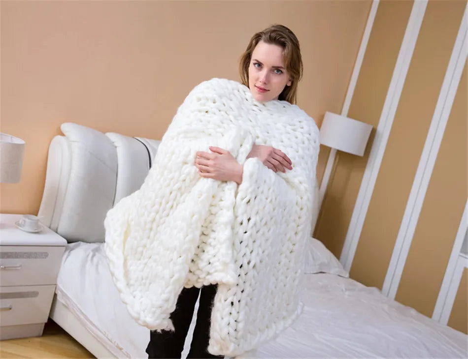 A woman holding a thick, white, chunky-knit yarn blanket in a bedroom.