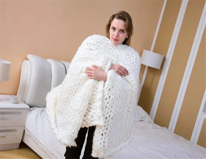 A woman holding a thick, white, chunky-knit yarn blanket in a bedroom.
