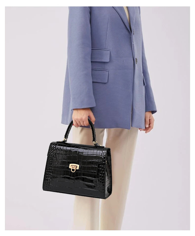 Black patent leather crocodile-pattern handbag with top handle, flap closure, and gold-tone clasp hardware.