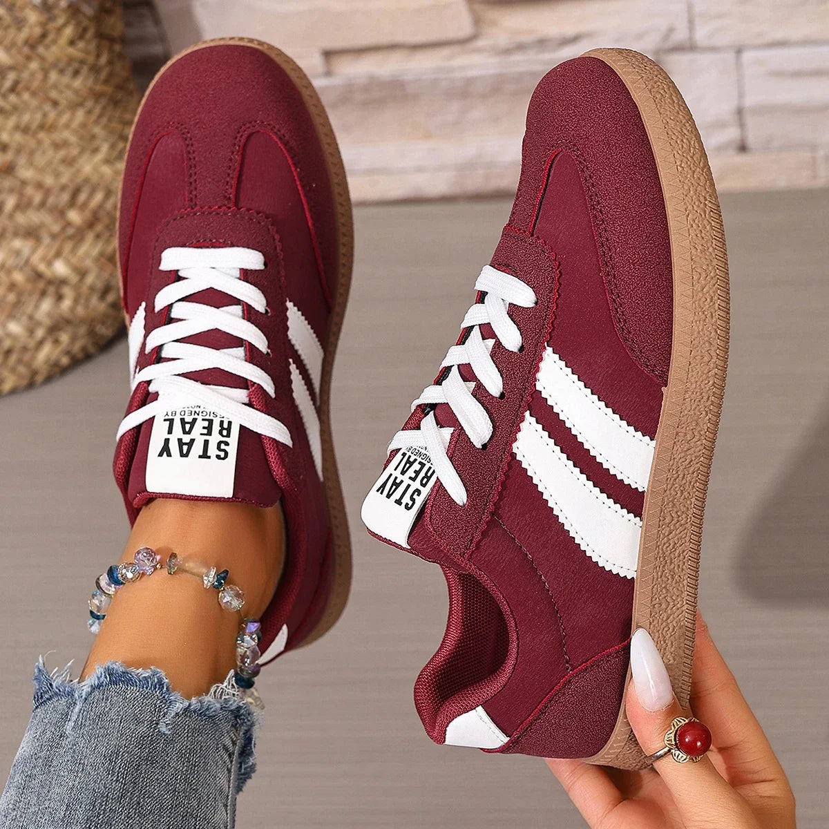 Maroon leather slip-on sneakers with white stripes, white laces, and gum soles for casual daily wear.