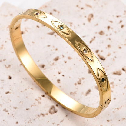 Gold stainless steel cuff bangle featuring engraved evil eye motifs with inlaid colorful crystals.