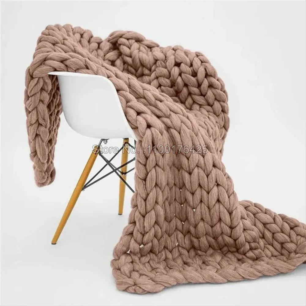 Chunky taupe knitted yarn blanket draped over a modern white chair with wooden legs.