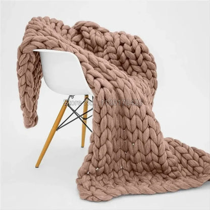 Chunky taupe knitted yarn blanket draped over a modern white chair with wooden legs.