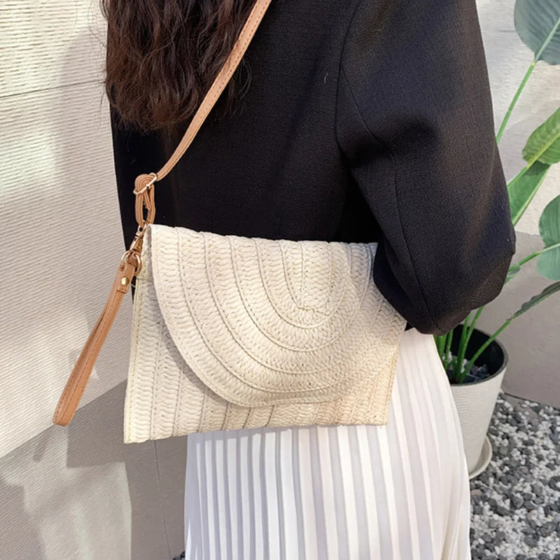 Beige woven straw envelope crossbody bag with an adjustable strap, ideal for a beach vacation.