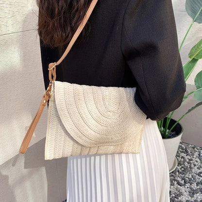 Beige woven straw envelope crossbody bag with an adjustable strap, ideal for a beach vacation.