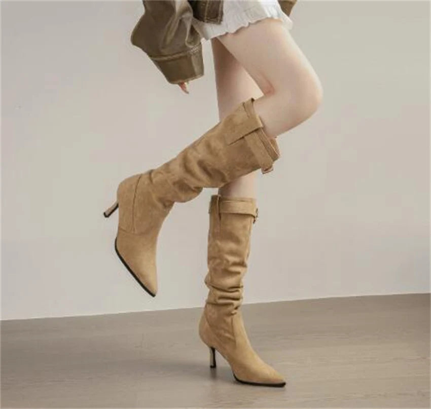 Tan suede pointed-toe knee-high boots with thin stiletto heels, slouchy shafts, and ankle buckle straps.