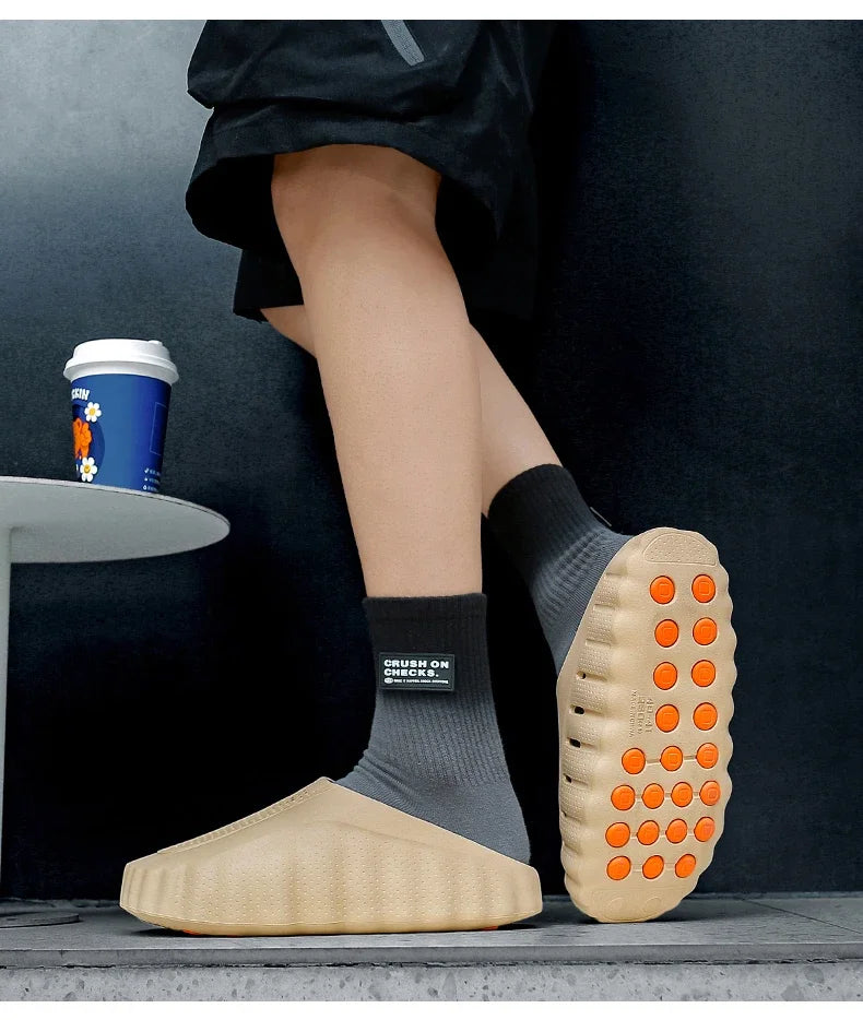 Tan slip-on sandals featuring a cushioned thick sole with orange circular grips for daily comfort.