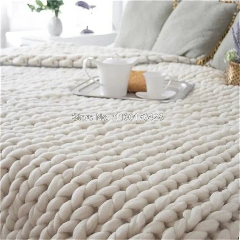 Thick grey chunky yarn hand-knitted throw blanket with a large braided texture, draped over a bed.