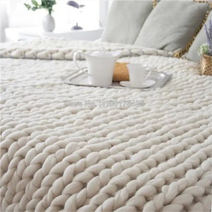 Thick grey chunky yarn hand-knitted throw blanket with a large braided texture, draped over a bed.