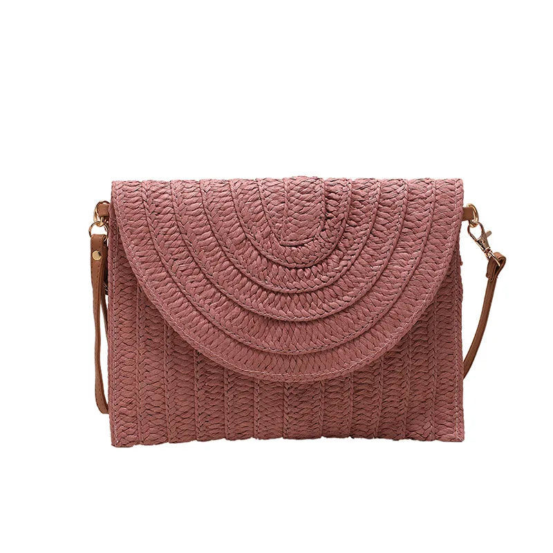 Dusty pink woven straw crossbody bag with an envelope flap and adjustable strap for beach outings.