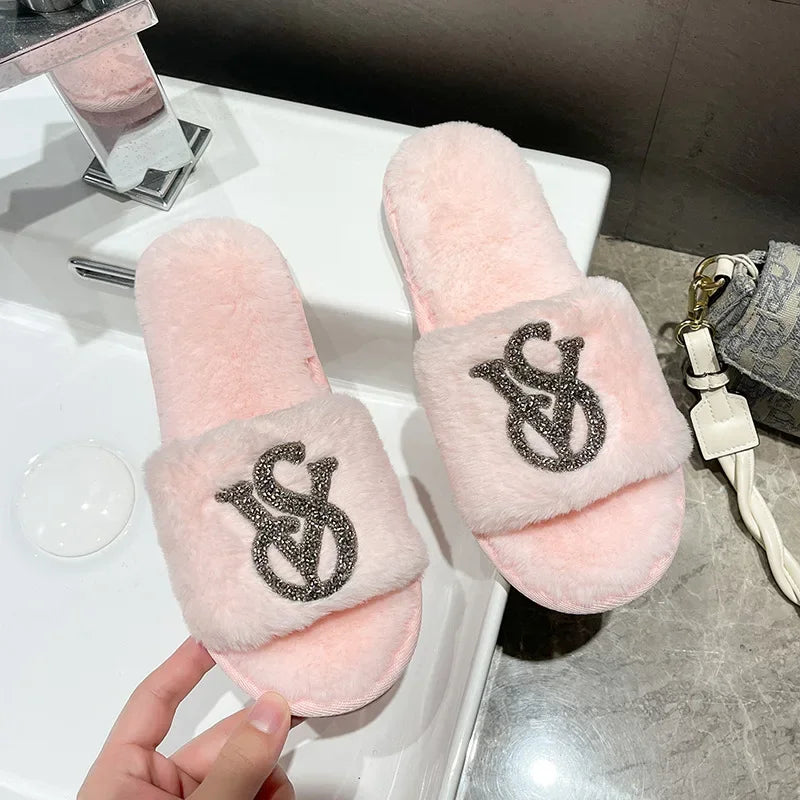 Light pink faux fur slippers with rhinestone logo detail and a non-slip sole for indoor wear.
