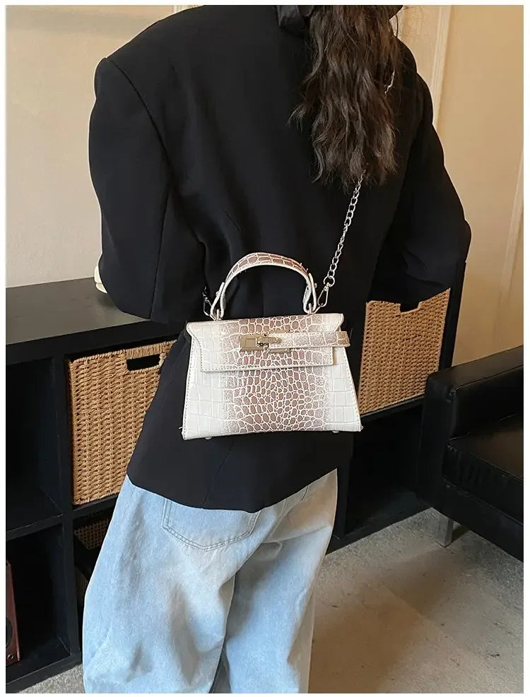 White and beige croc-print structured diaper bag with a silver chain strap for parents on the go.