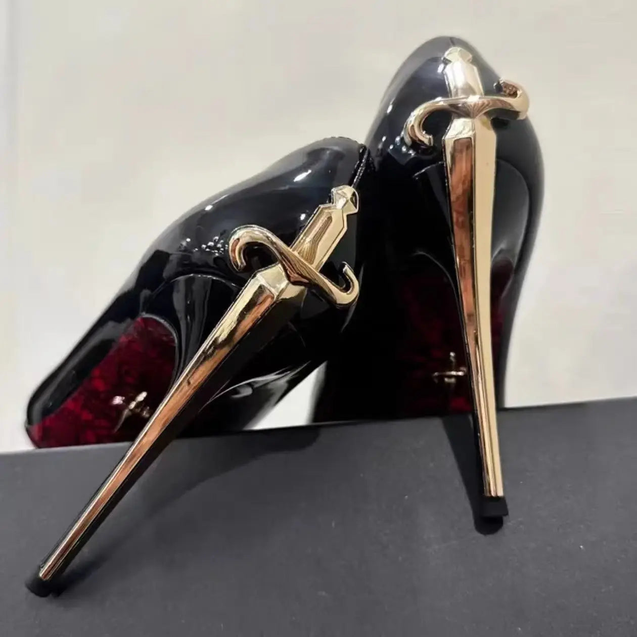 Black PU stiletto pumps with gold sword-shaped heels for formal wear.
