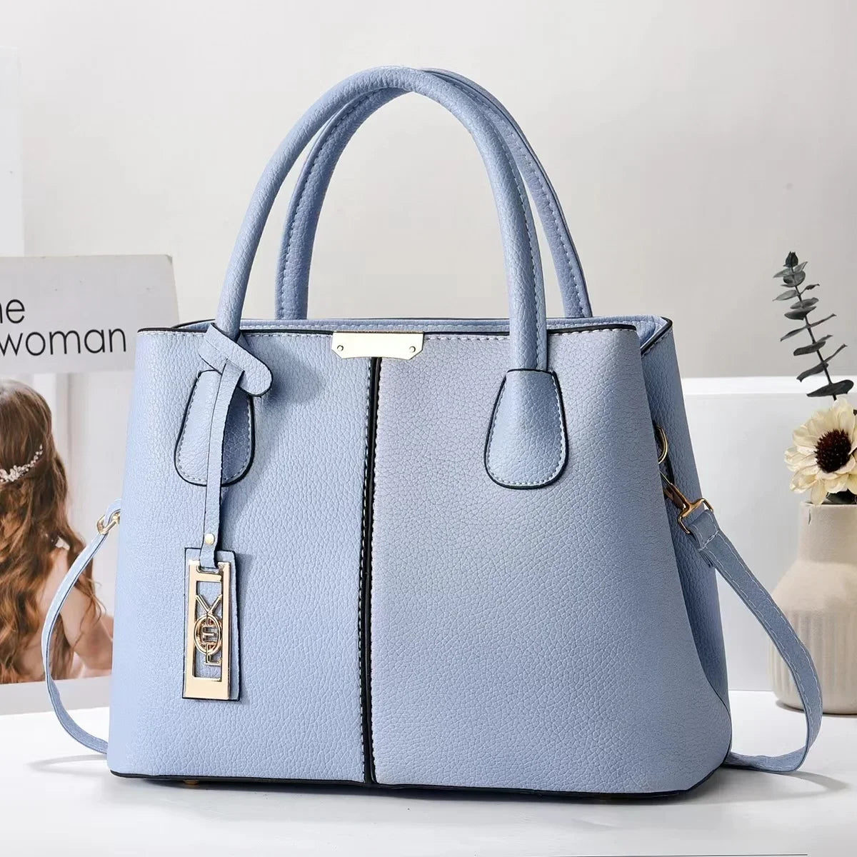 Light blue faux leather structured tote bag with zip closure and adjustable strap for everyday use.