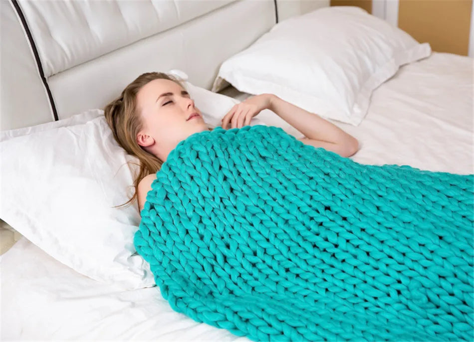 A woman lies in bed, covered by a turquoise, chunky hand-knitted roving yarn blanket.