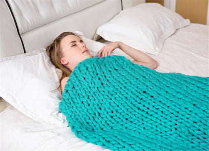 A woman lies in bed, covered by a turquoise, chunky hand-knitted roving yarn blanket.