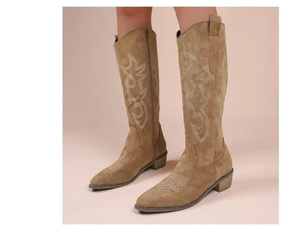 Tan suede western cowboy boots with pointed toes, block heels, and white contrast embroidery.