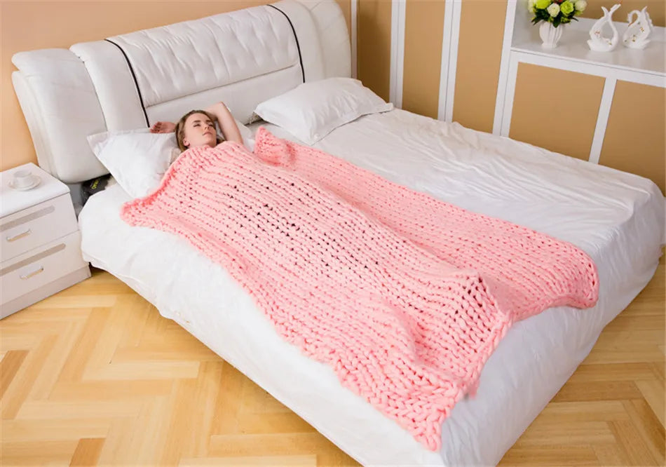 A thick, chunky hand-knitted pink yarn roving blanket draped over a person lying on a white bed.
