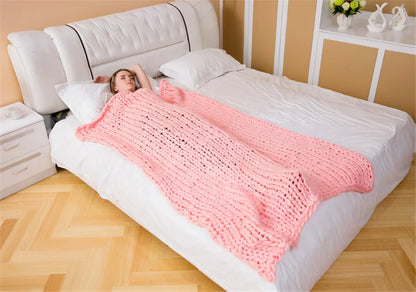 A thick, chunky hand-knitted pink yarn roving blanket draped over a person lying on a white bed.