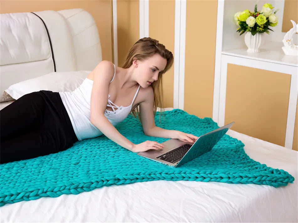 Teal chunky knit yarn blanket, thick handmade throw draped on a bed with a person using a laptop.