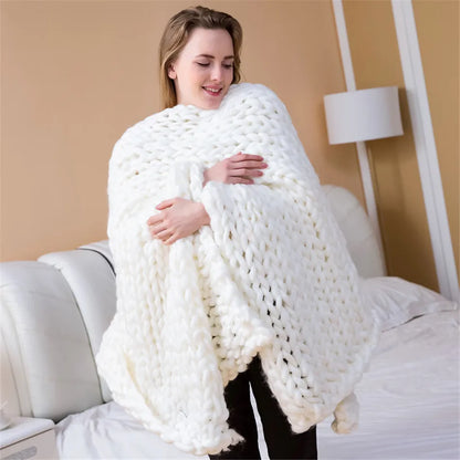 A woman wrapped in a thick, white, chunky-knit yarn blanket indoors.