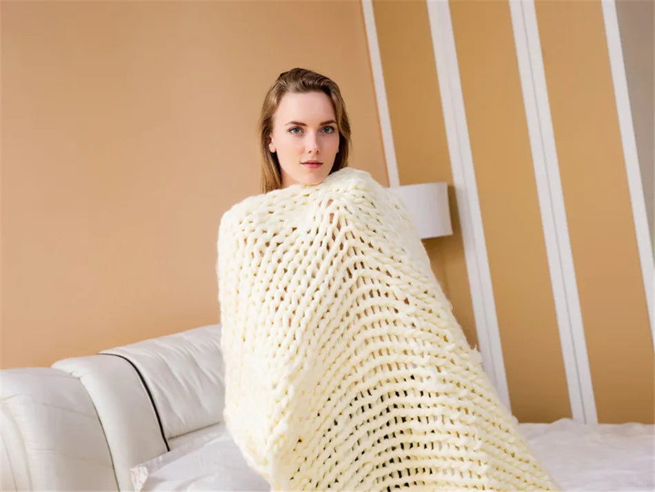 A woman wrapped in a thick, cream-colored, chunky knit yarn blanket.