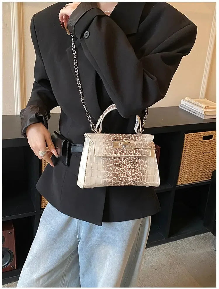 Beige crocodile-embossed faux leather crossbody bag with a metal chain strap for carrying baby essentials.