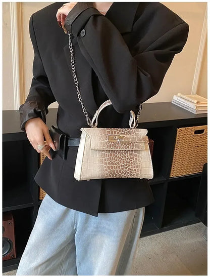 Beige crocodile-embossed faux leather crossbody bag with a metal chain strap for carrying baby essentials.