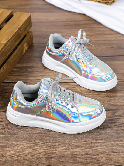 Pair of metallic holographic lace-up sneakers with chunky white soles and shimmering silver laces on wood.