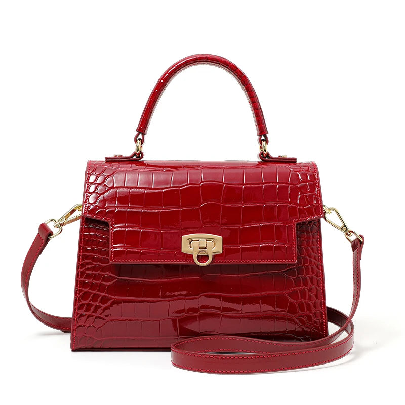 Red glossy crocodile-pattern leather handbag with a top handle, gold closure, and crossbody strap.