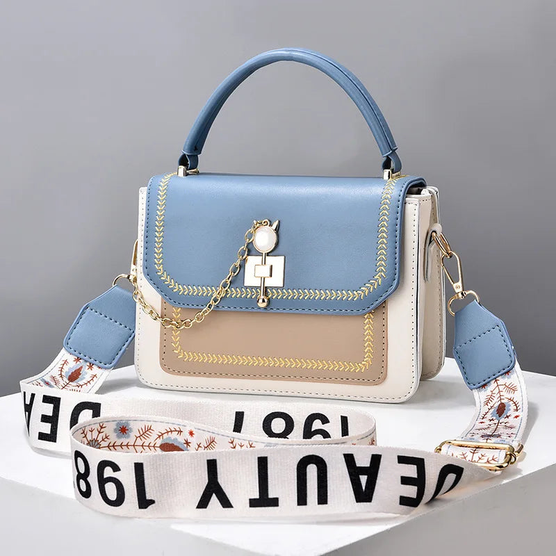 Blue, tan, and white leather handbag with top handle, gold chain charm, and wide patterned strap.
