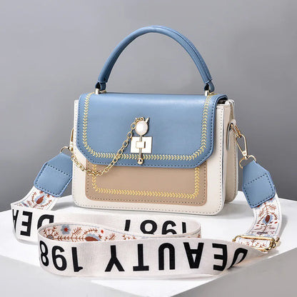 Blue, tan, and white leather handbag with top handle, gold chain charm, and wide patterned strap.