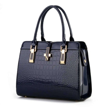 Glossy navy blue crocodile-pattern leather handbag with gold hardware, dual top handles, and a central clasp.