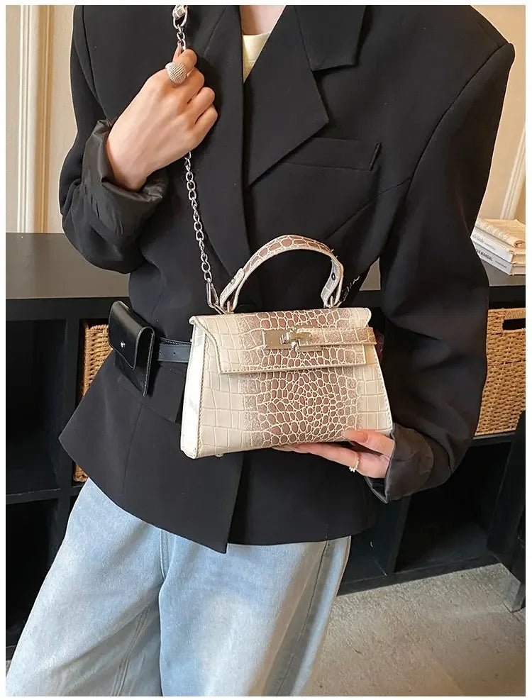 Beige faux leather structured satchel with a crocodile texture and metal closure for carrying baby essentials.